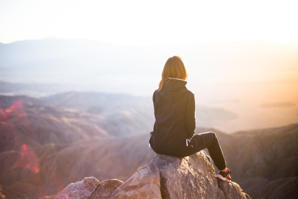 woman sitting on a rock, facing away, looking toward the sunset